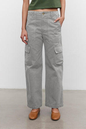 A person wearing the stylish MAKAYLA PANT by Velvet by Graham & Spencer, featuring handy cargo pockets, pairs them with a green top and brown shoes while standing against a white background. This versatile wardrobe choice is both chic and practical for any occasion.