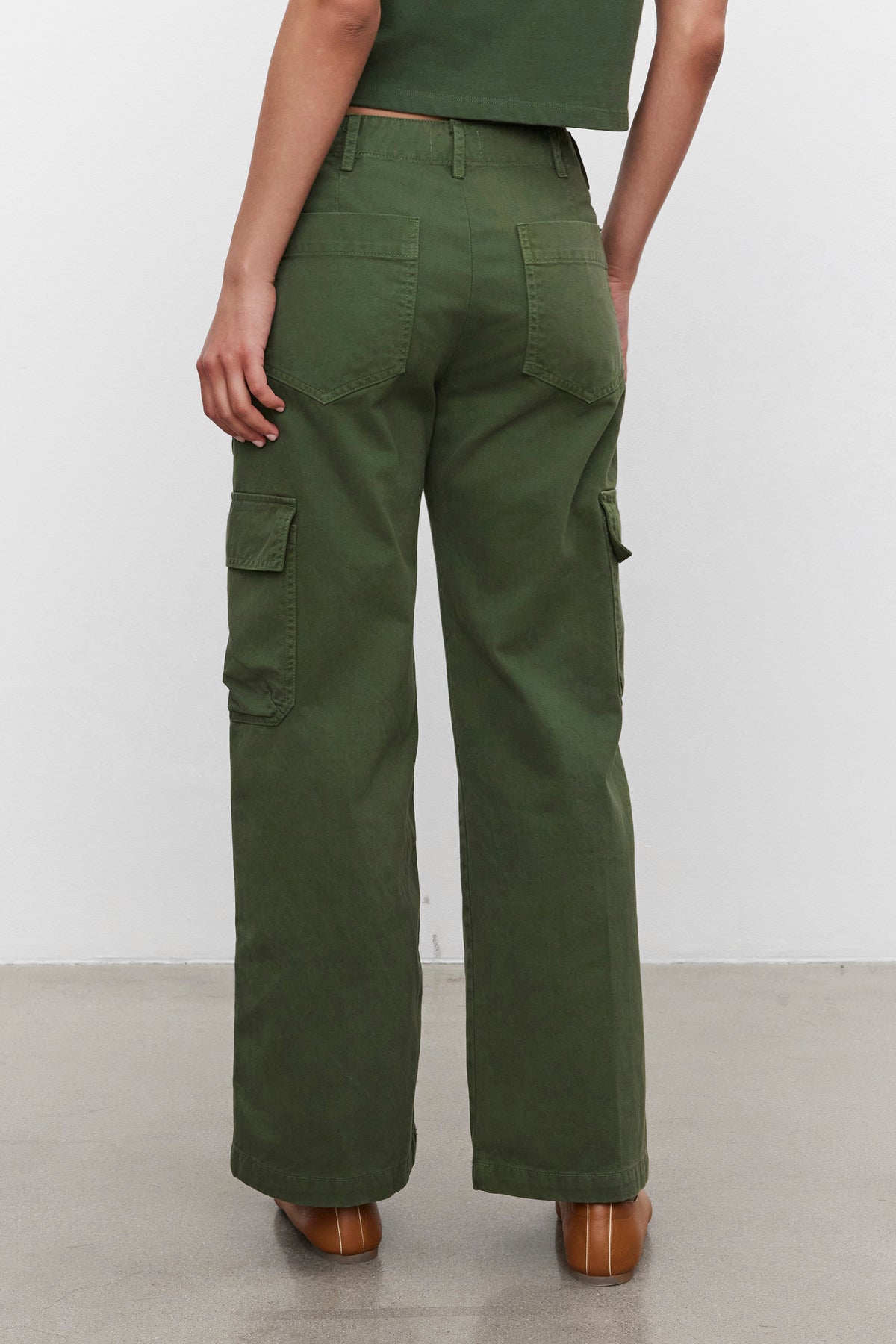 Person wearing MAKAYLA PANT by Velvet by Graham & Spencer in green sanded cotton twill and a green top, facing away. The versatile wardrobe features large cargo flap pockets on the sides and back.