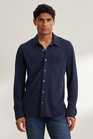 A person wearing a navy blue GIORGIO PIQUE BUTTON-UP SHIRT by Velvet by Graham & Spencer and blue jeans stands against a neutral background.