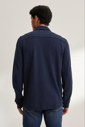 A man wearing the GIORGIO PIQUE BUTTON-UP SHIRT in navy blue from Velvet by Graham & Spencer, paired with jeans, stands with his back to the camera against a neutral background.