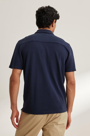 A man stands against a neutral background, facing away, wearing a MARTYN PIQUE BUTTON-UP SHIRT by Velvet by Graham & Spencer in navy paired with beige pants.