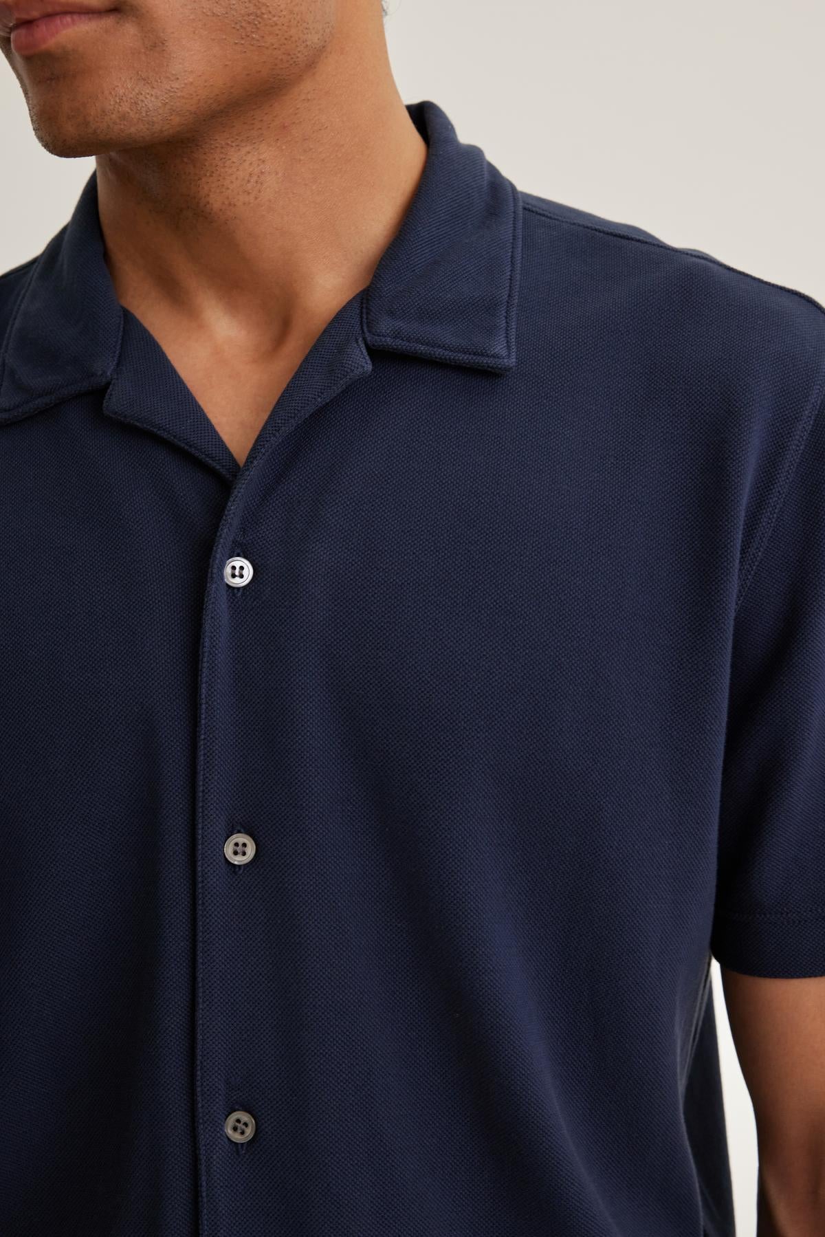 A person wearing the MARTYN PIQUE BUTTON-UP SHIRT from Velvet by Graham & Spencer, featuring a navy blue color, short sleeves, and a collar.