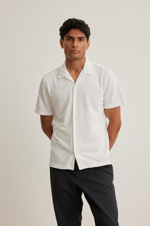 Person standing against a plain backdrop, wearing the short-sleeve MARTYN PIQUE BUTTON-UP SHIRT by Velvet by Graham & Spencer and dark pants.