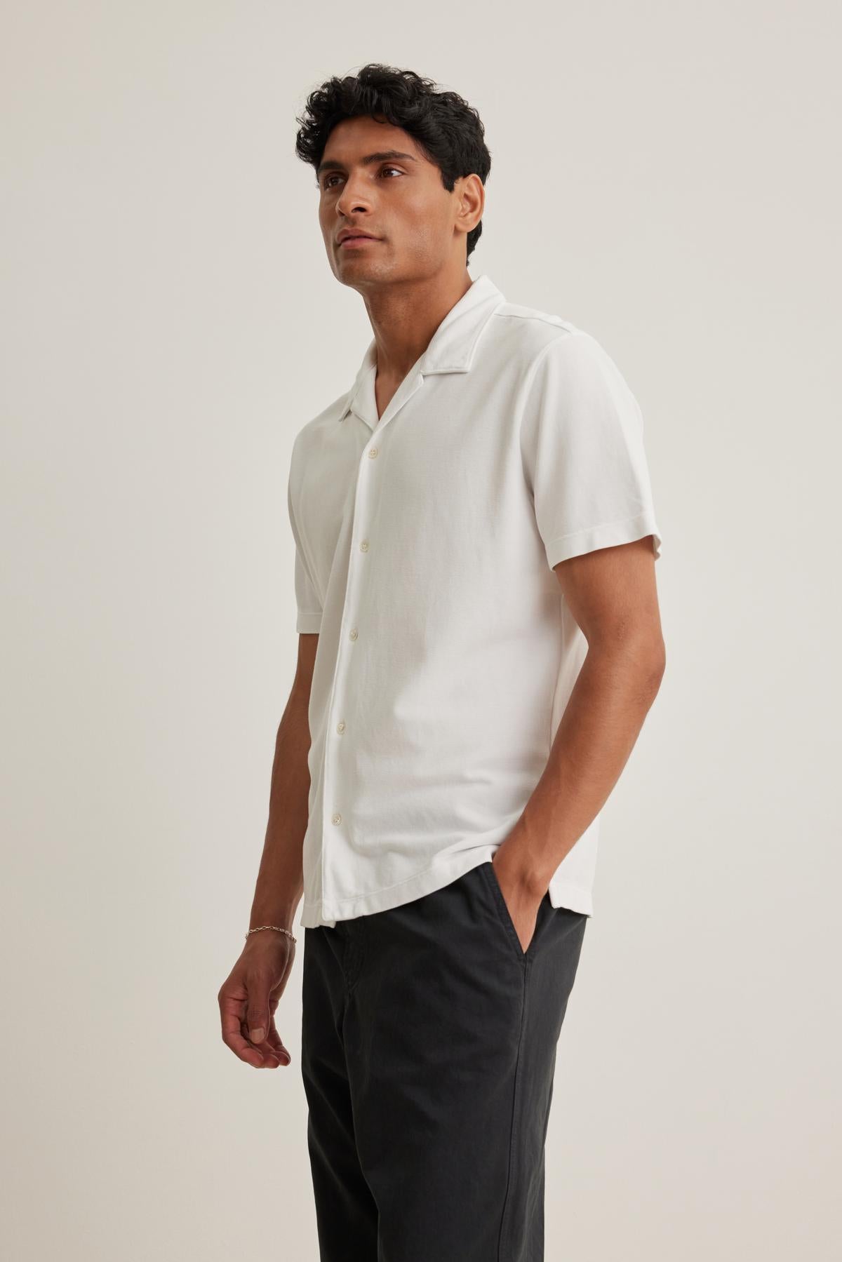 Someone wearing the MARTYN PIQUE BUTTON-UP SHIRT by Velvet by Graham & Spencer and dark pants stands with one hand in their pocket against a neutral background.