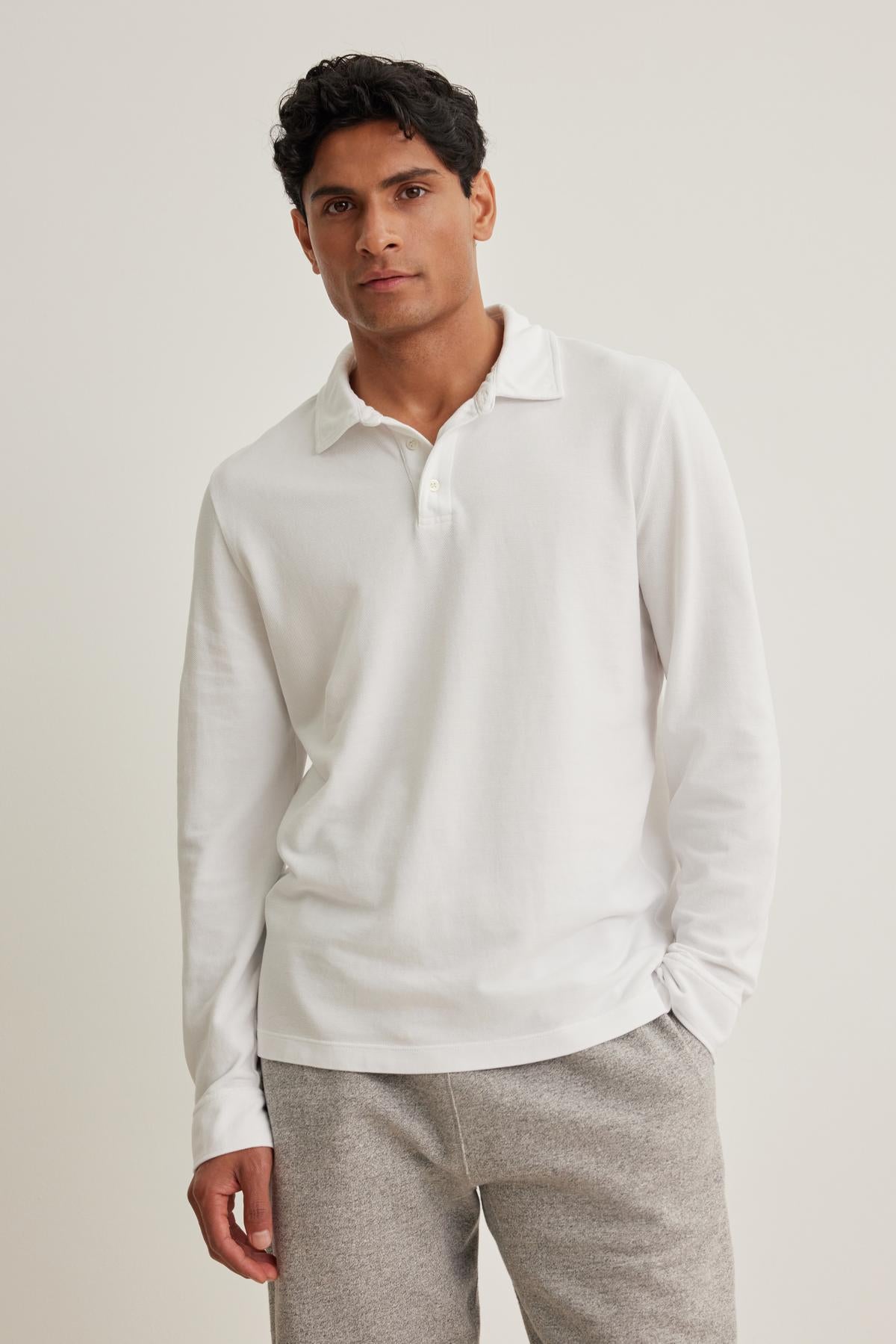 A person stands against a plain background wearing Velvet by Graham & Spencer's SACHA PIQUE POLO, a white long-sleeve shirt, paired with gray pants.