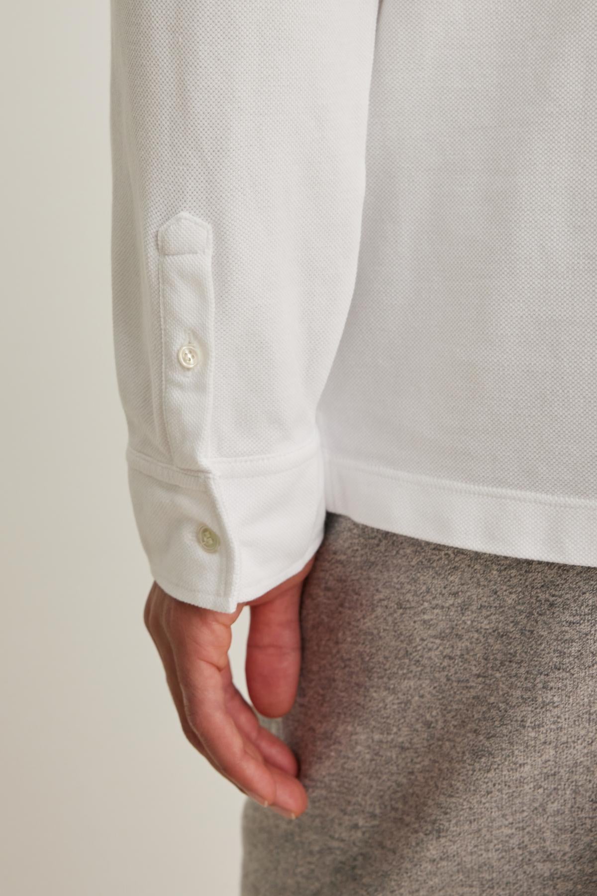 A person wearing the SACHA PIQUE POLO by Velvet by Graham & Spencer with gray pants, emphasizing the shirt's buttoned cuff.