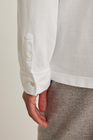 A person wearing the SACHA PIQUE POLO by Velvet by Graham & Spencer with gray pants, emphasizing the shirt's buttoned cuff.