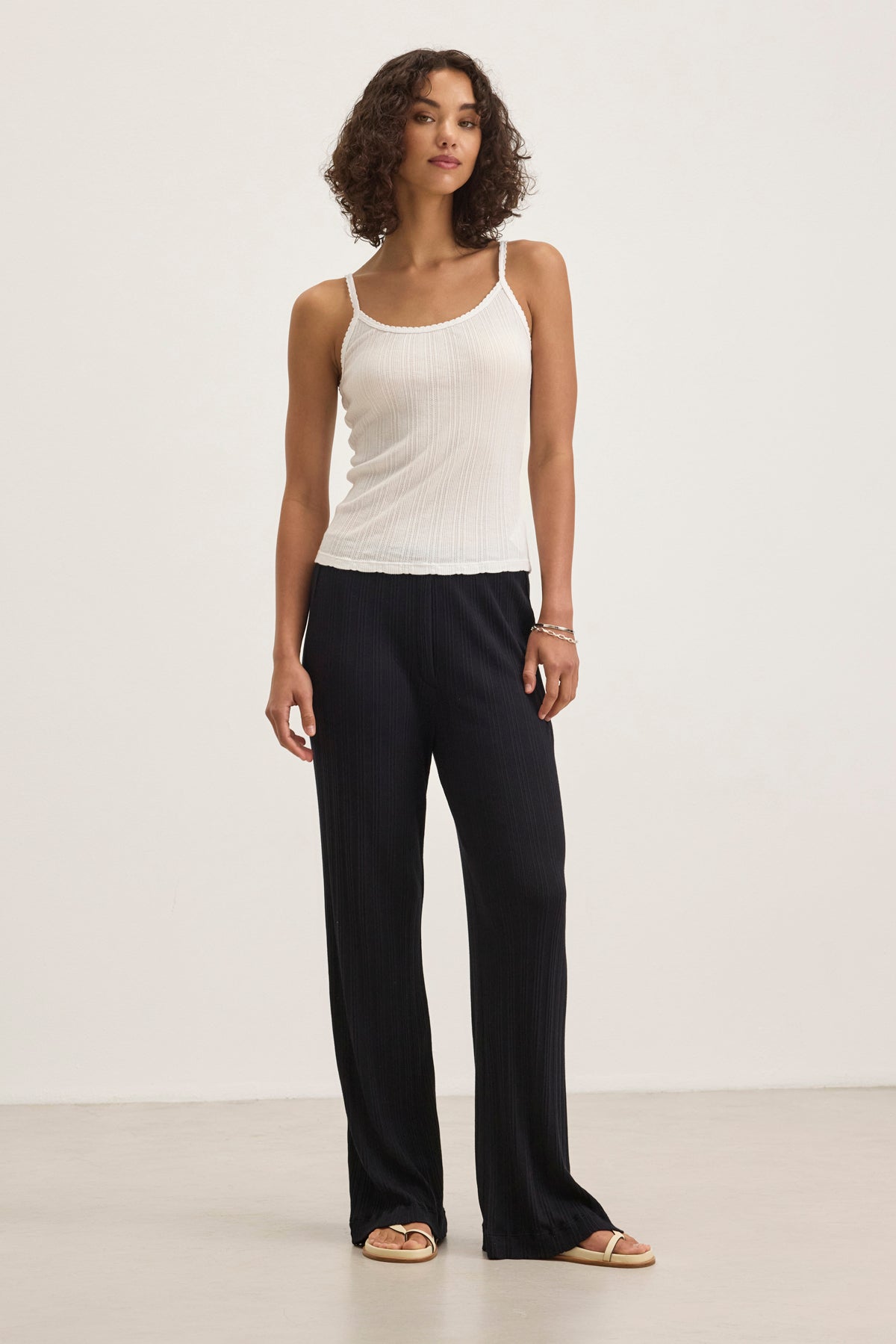 A person models the flattering fit of ALEMI POINTELLE PANT from Velvet by Graham & Spencer, pairing sleek black cotton-modal wide-leg pants with a white sleeveless top featuring ribbed pointelle accents against a neutral backdrop.-38802035114177