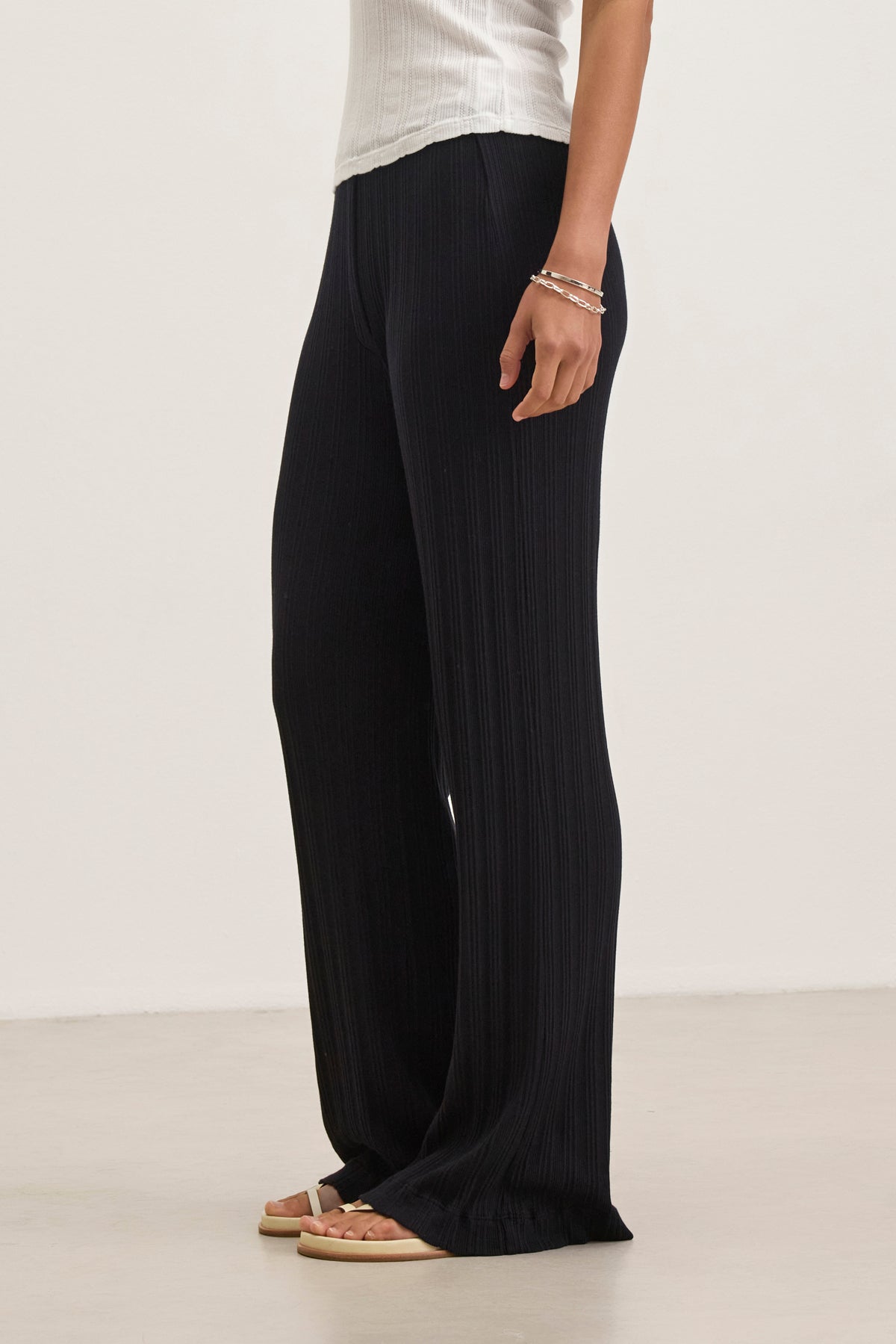 A person is wearing the Velvet by Graham & Spencer ALEMI POINTELLE PANT, featuring a white top with ribbed pointelle accents, black wide-leg pants offering a flattering fit, and sandals.-38802035081409