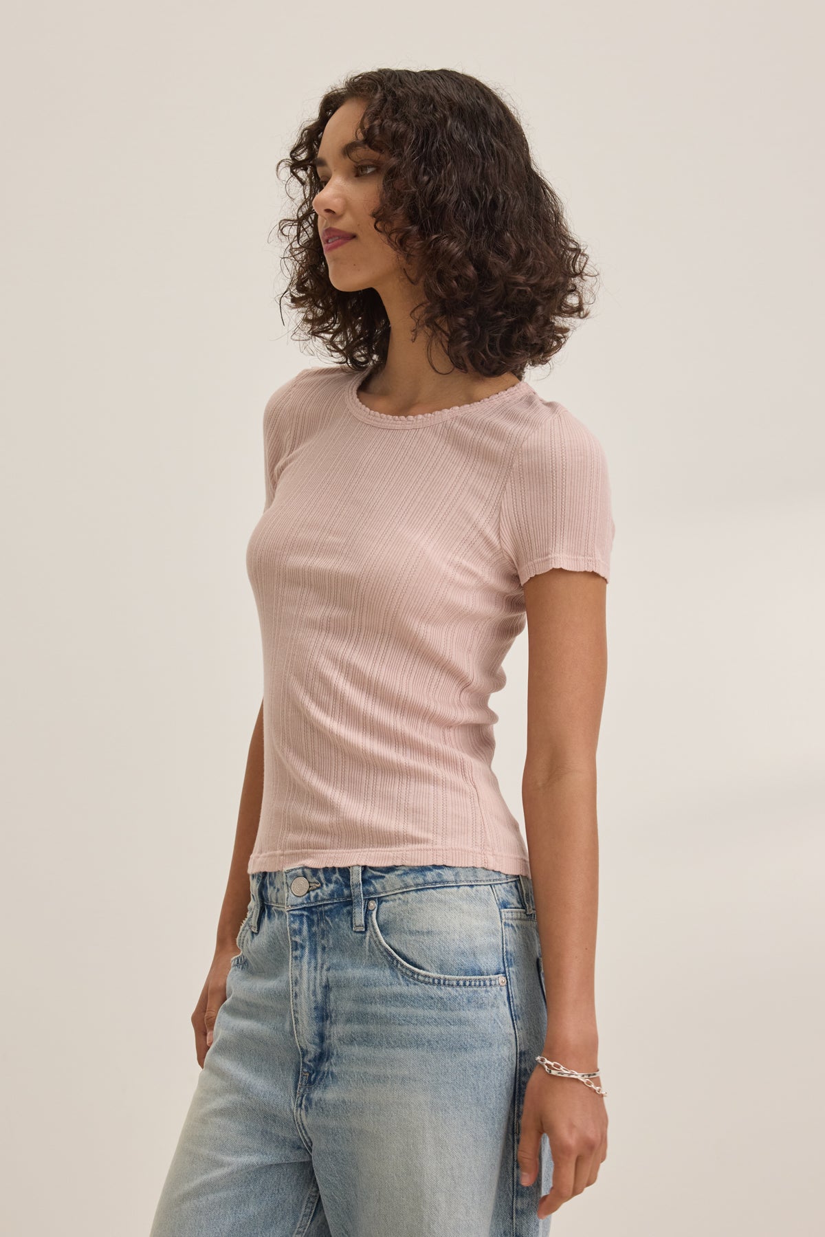 A person is wearing the ENATI POINTELLE TEE by Velvet by Graham & Spencer, a light pink ribbed shirt with scalloped edges, paired with blue jeans against a plain background.