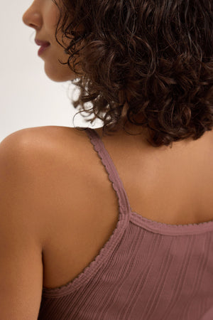 A woman with short curly hair is seen from behind wearing the Velvet by Graham & Spencer INIKU POINTELLE TANK TOP, a mauve cotton-modal blend tank with spaghetti straps.