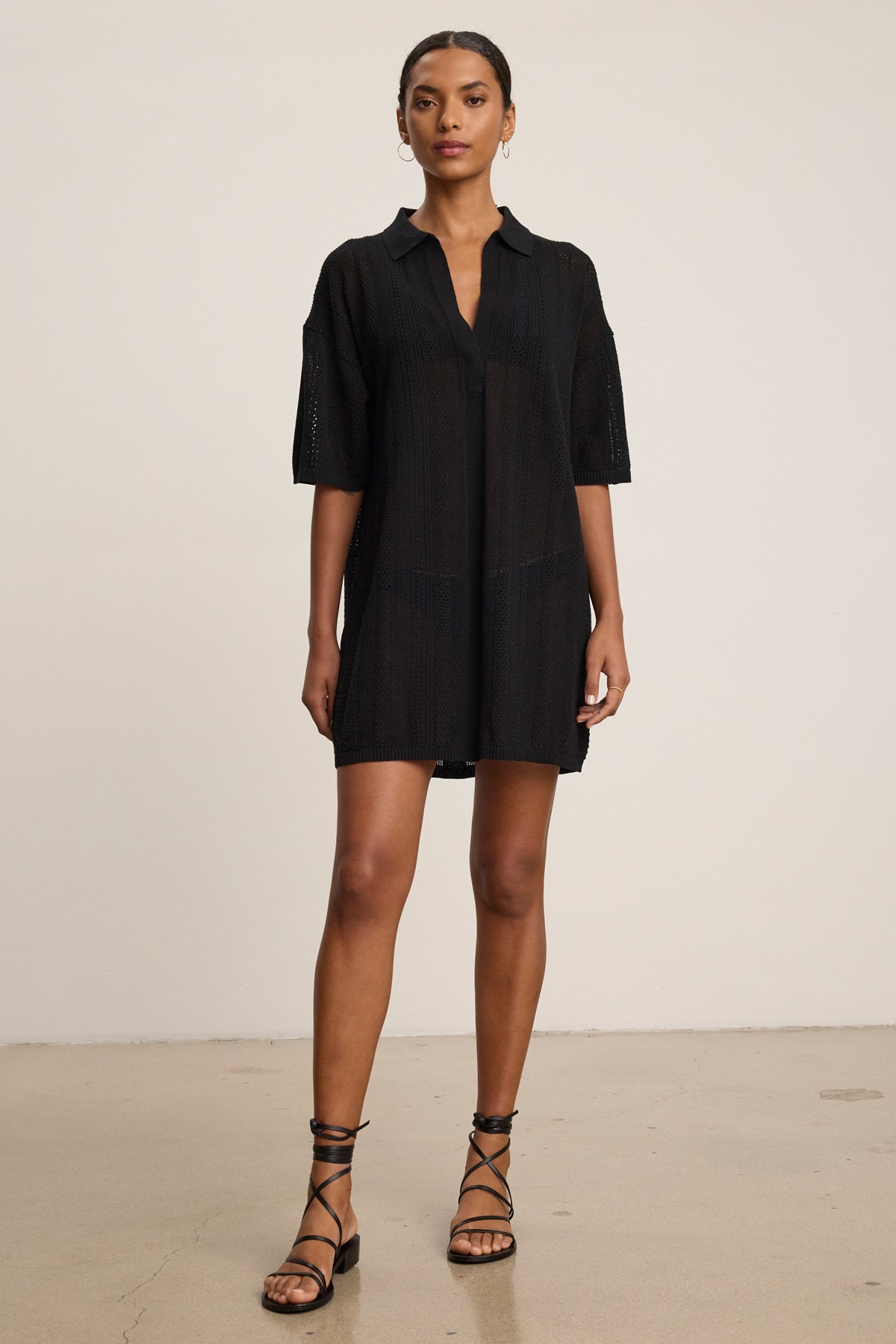 A woman stands indoors in the MILA POINTELLE LACE DRESS by Velvet by Graham & Spencer and black strappy sandals, posed against a plain light background—an effortless addition to any summer wardrobe.