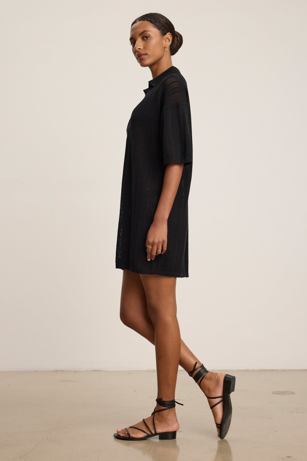 A woman stands in profile wearing the MILA POINTELLE LACE DRESS by Velvet by Graham & Spencer and black strappy sandals against a plain light background—an ideal choice for a versatile summer wardrobe.-39488809959617