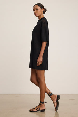 A woman stands in profile wearing the MILA POINTELLE LACE DRESS by Velvet by Graham & Spencer and black strappy sandals against a plain light background—an ideal choice for a versatile summer wardrobe.