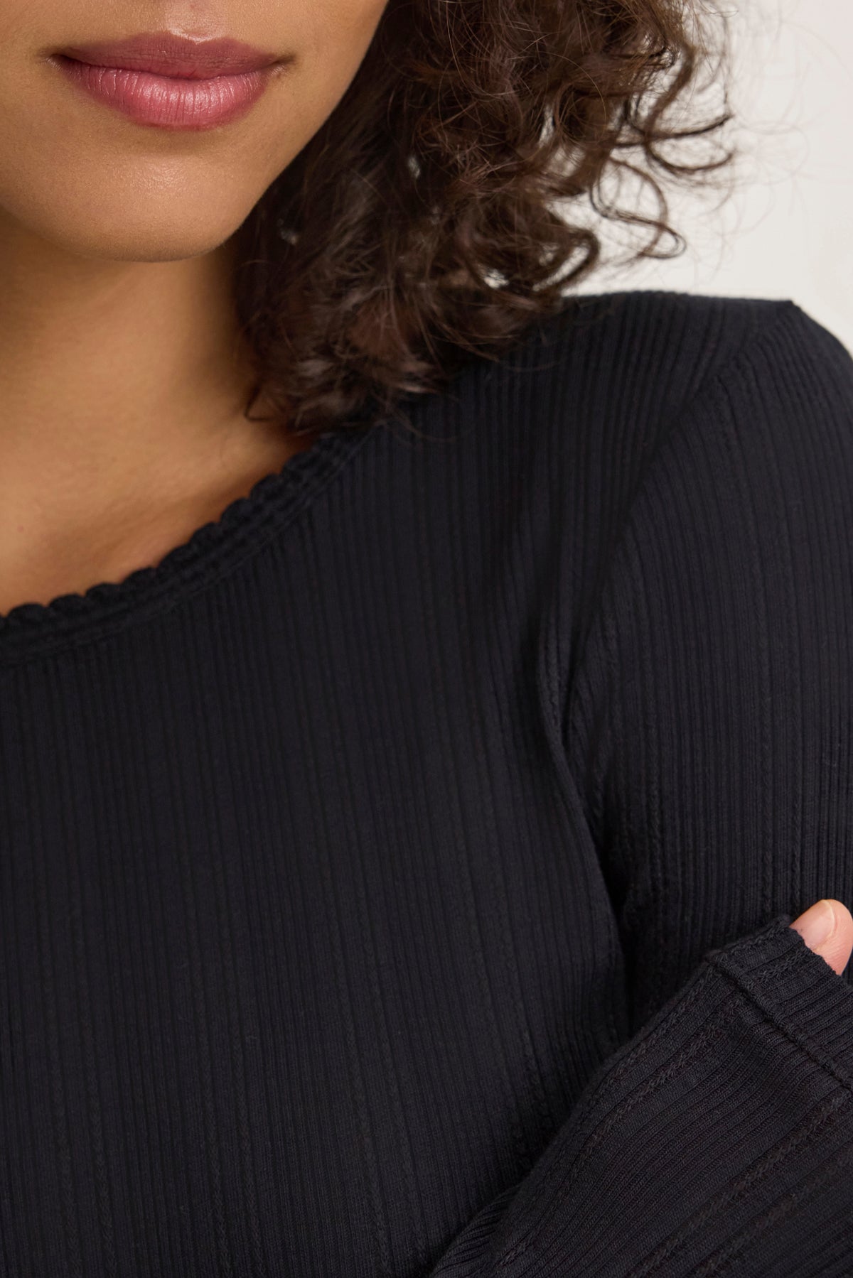 A person with curly hair wears a black MAURI POINTELLE TEE by Velvet by Graham & Spencer, seen from the shoulders up.-38820767531201