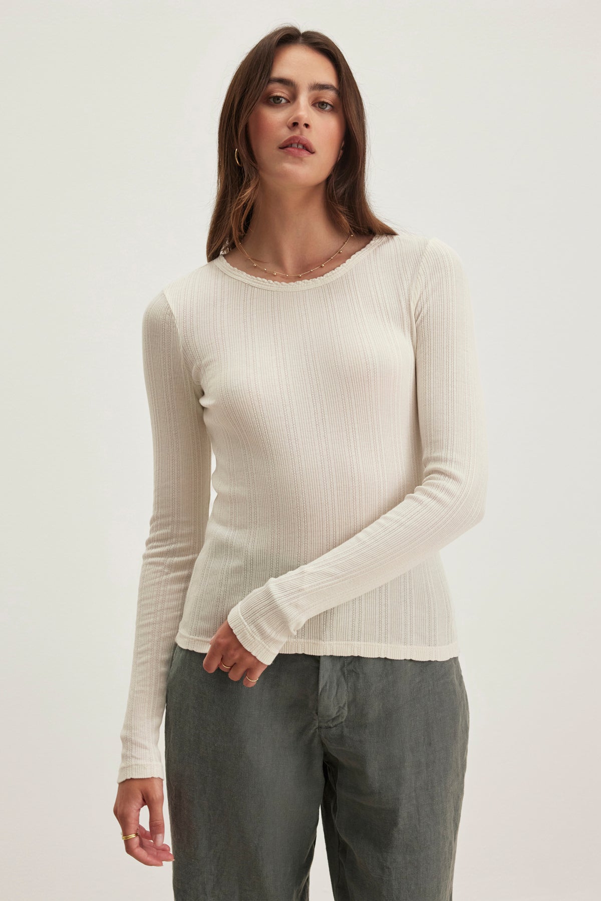 A person wearing a light-colored MAURI POINTELLE TEE by Velvet by Graham & Spencer and dark pants stands against a plain white background.-38820768055489