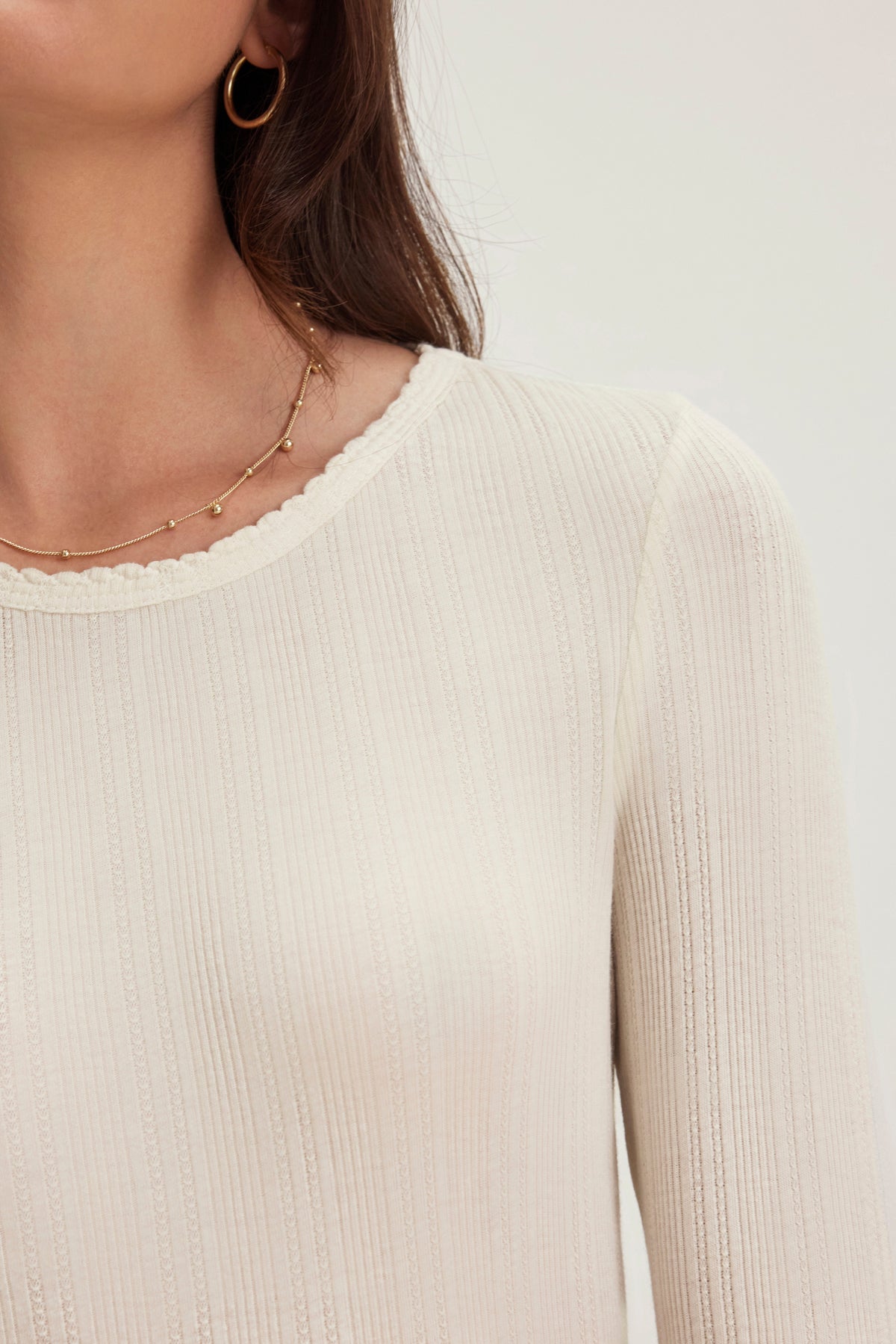 Someone wearing a MAURI POINTELLE TEE by Velvet by Graham & Spencer, complemented with gold hoop earrings and a delicate gold necklace featuring small beads.