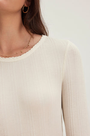 Someone wearing a MAURI POINTELLE TEE by Velvet by Graham & Spencer, complemented with gold hoop earrings and a delicate gold necklace featuring small beads.