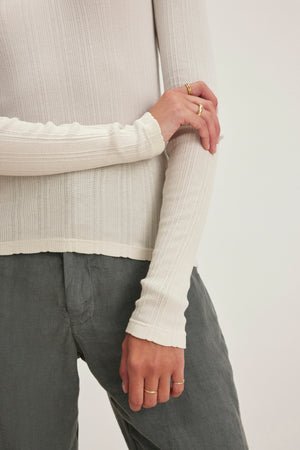 A person in a Velvet by Graham & Spencer MAURI POINTELLE TEE and gray pants crosses their arms, showing two gold rings on their right hand.