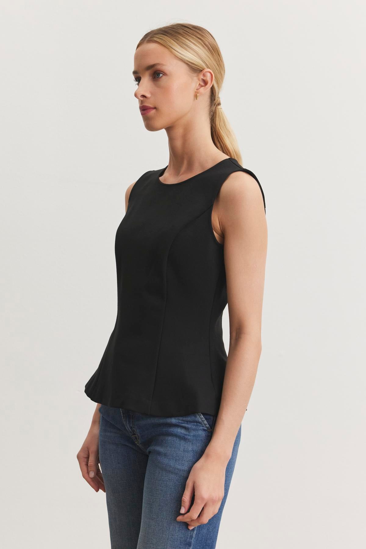 A person with blonde hair tied back, wearing the FELICITEE PONTE TOP by Velvet by Graham & Spencer and blue jeans, stands against a plain white background.