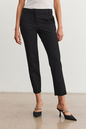 A woman stands on a polished floor, wearing the JAY PONTE PANTS by Velvet by Graham & Spencer, along with black pointed-toe heels accented with pearl straps.
