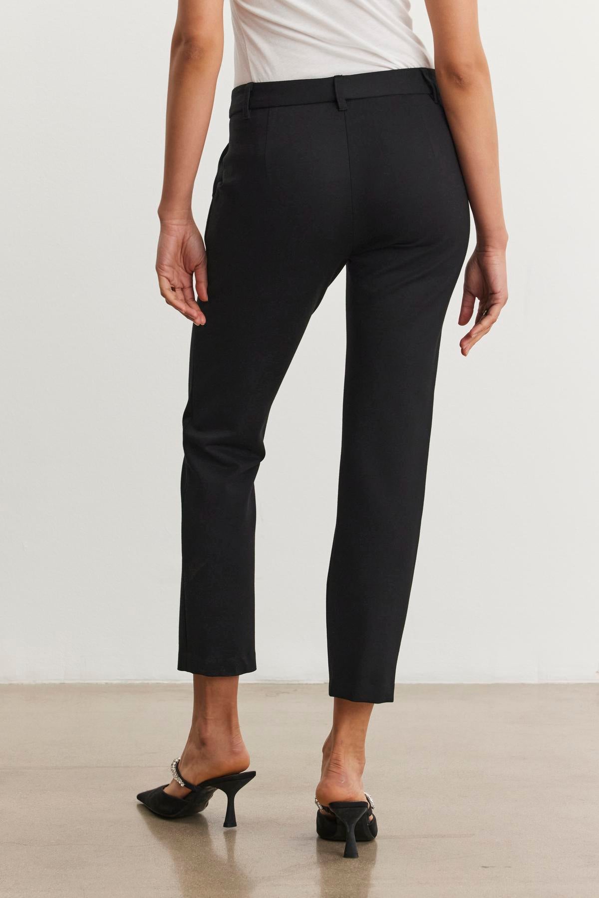 A person wearing the JAY PONTE PANT from Velvet by Graham & Spencer, featuring a straight leg silhouette, and black heeled shoes is standing on a beige floor, facing away.
