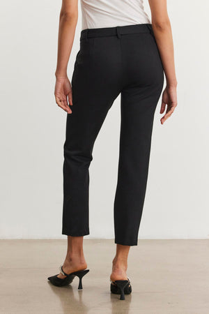 A person wearing the JAY PONTE PANT from Velvet by Graham & Spencer, featuring a straight leg silhouette, and black heeled shoes is standing on a beige floor, facing away.