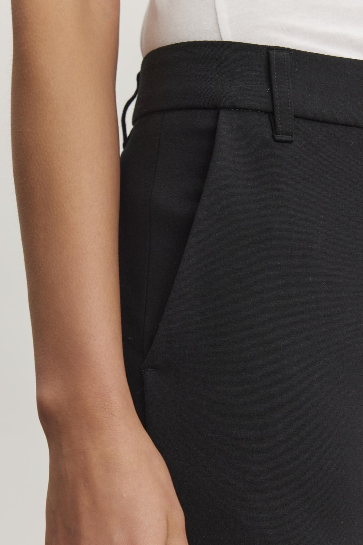 Close-up of a person wearing the JAY PONTE PANT by Velvet by Graham & Spencer, in black ponte fabric, with their right hand resting beside a side pocket.