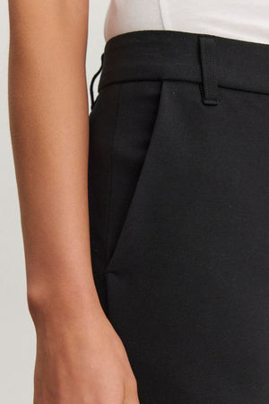Close-up of a person wearing the JAY PONTE PANT by Velvet by Graham & Spencer, in black ponte fabric, with their right hand resting beside a side pocket.