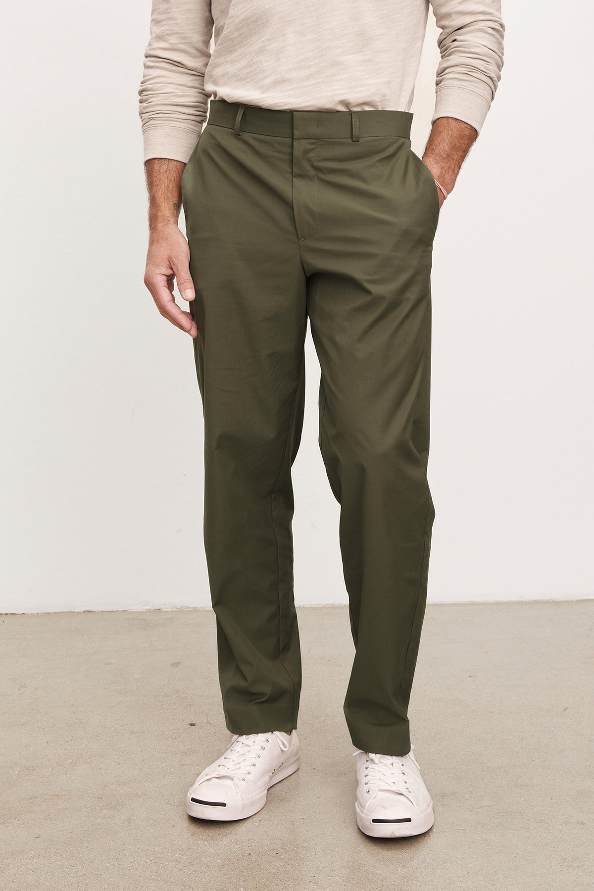 A person wears Velvet by Graham & Spencer's STING POPLIN PANT in olive green cotton poplin, paired with a light beige long-sleeve shirt and white sneakers, standing on a light floor—an effortlessly versatile wardrobe staple.