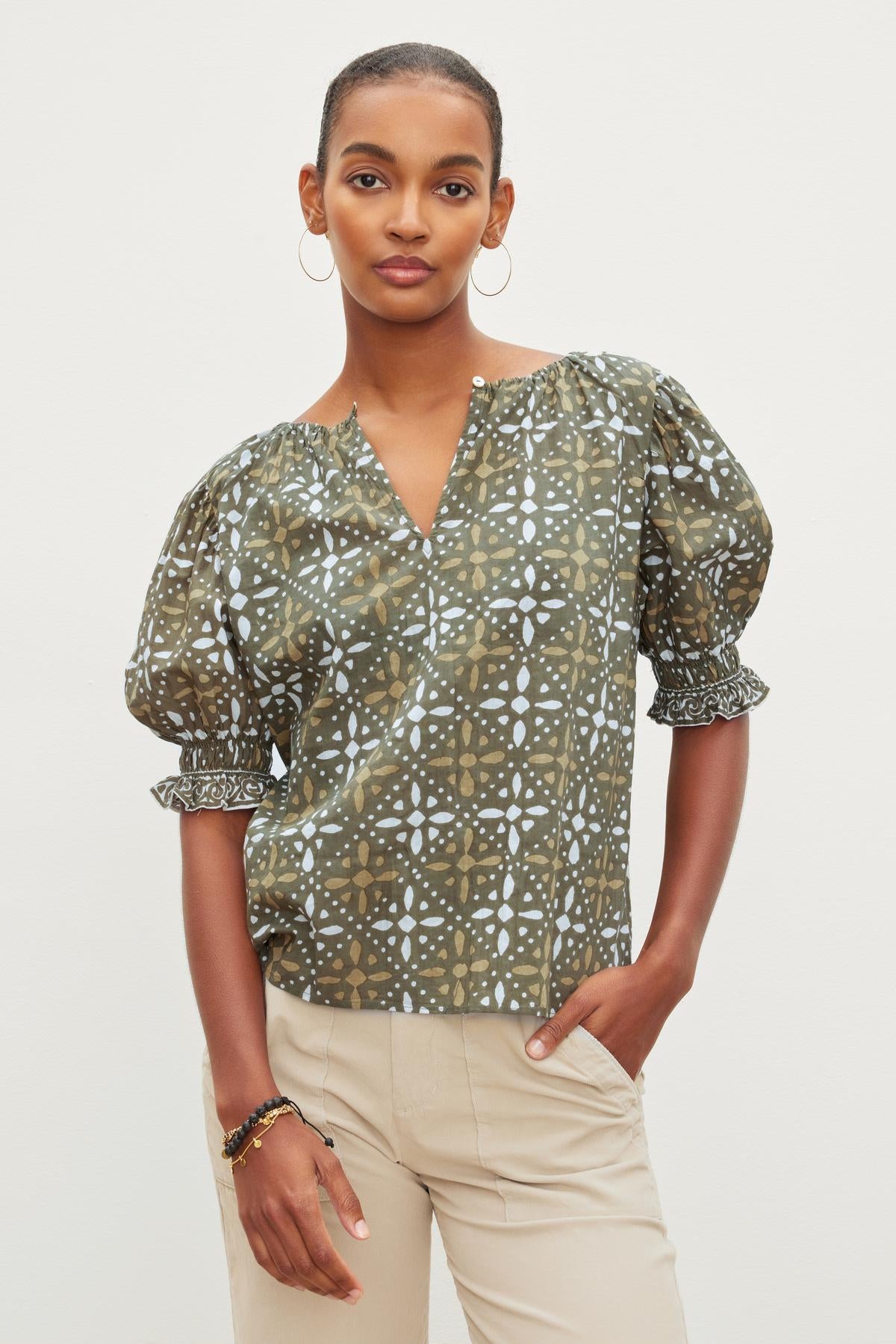 The model is wearing a Velvet by Graham & Spencer ALEX PRINTED BLOUSE with a puff sleeve and tan pants.-26799971729601