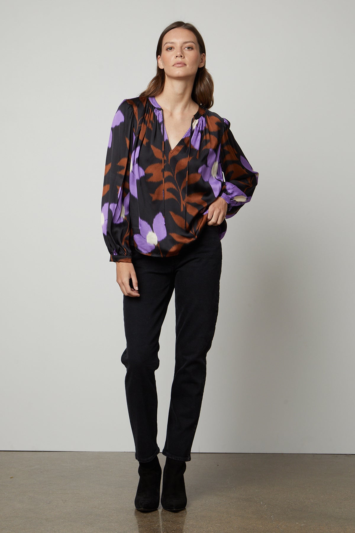 The model is wearing a black ISRA PRINTED V-NECK BLOUSE by Velvet by Graham & Spencer with a modern print of purple and black floral design.