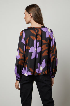 The back view of a woman wearing the Velvet by Graham & Spencer ISRA PRINTED V-NECK BLOUSE with purple flowers.
