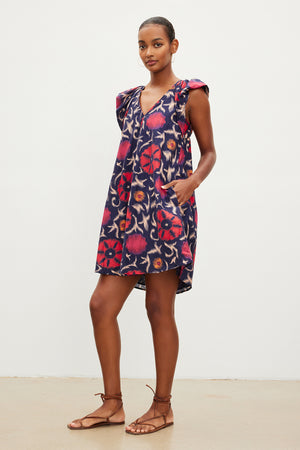 The model is wearing a Velvet by Graham & Spencer JENNA PRINTED SILK COTTON VOILE DRESS with ruffles and sandals.