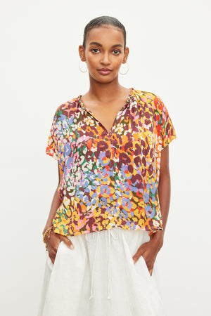 A woman wearing a Velvet by Graham & Spencer TRIXY PRINTED COCOON TOP and white pants.