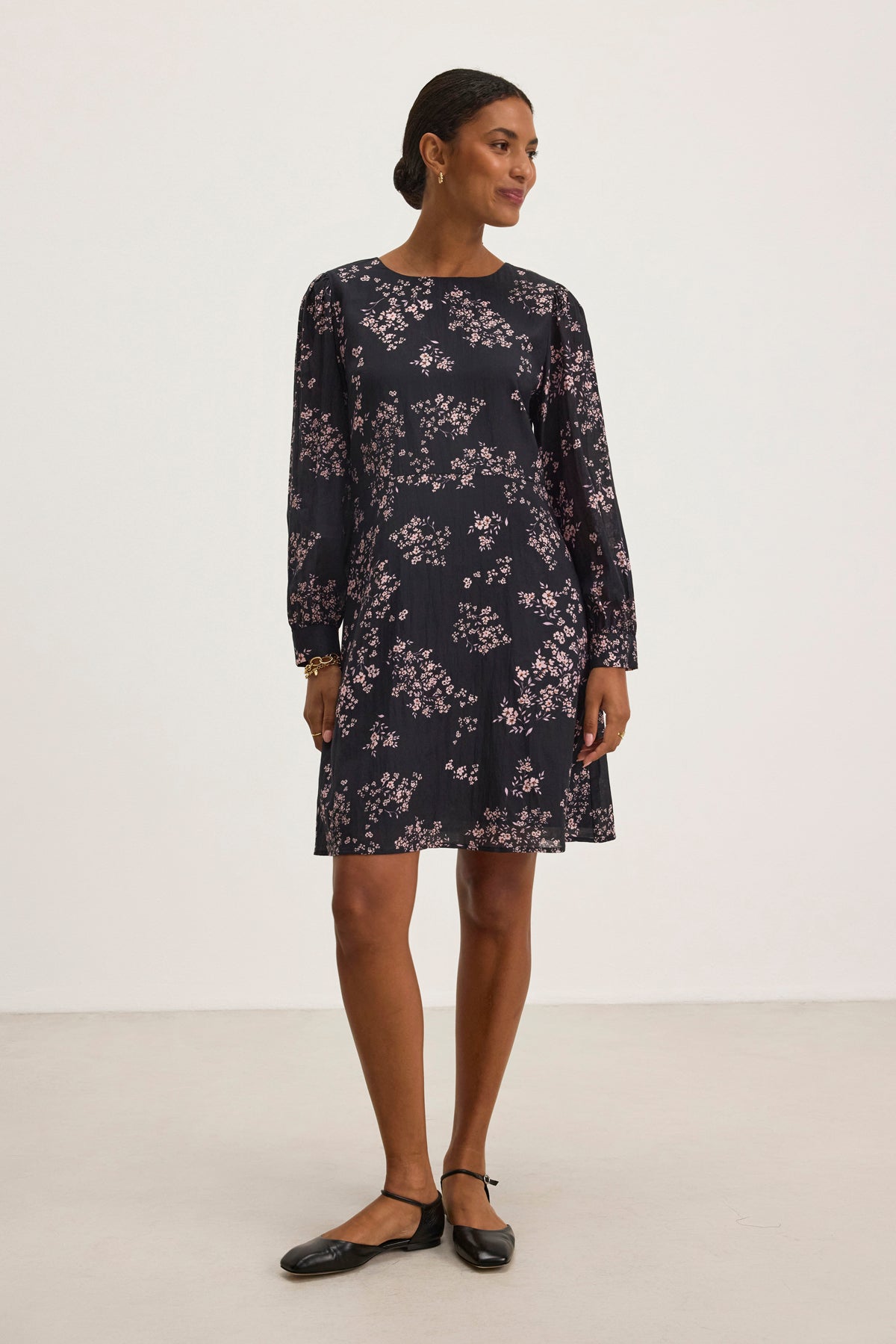 A woman in an elegant CELINA DRESS by Velvet by Graham & Spencer stands on a light background, facing slightly to the right, wearing black flats.