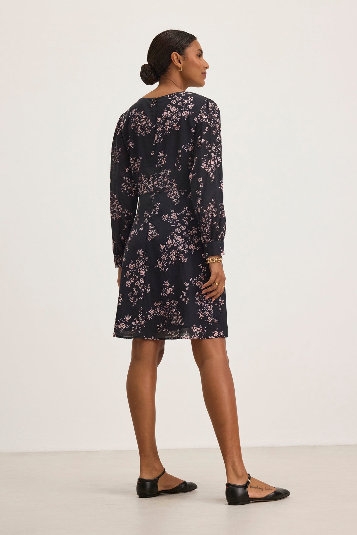 In a minimal setting, someone in the CELINA DRESS by Velvet by Graham & Spencer, an elegant dark floral cotton-viscose dress, pairs it with black flats while facing away.