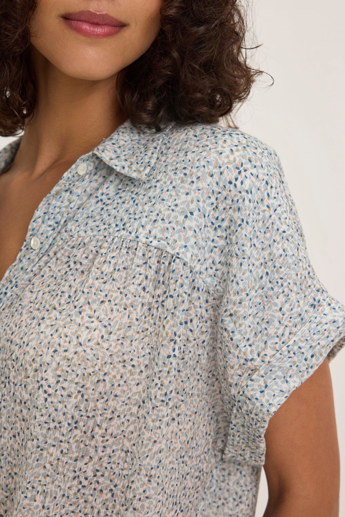 A person wears the Velvet by Graham & Spencer TIGE PRINTED CRINKLE COTTON GAUZE TOP, featuring a relaxed collar and button front. The cropped image shows their shoulder and part of their face against a plain background, highlighting the top's easygoing style.-38957723156673