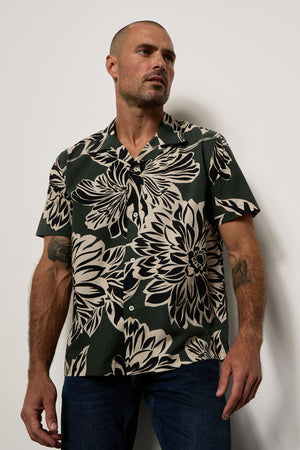A man in a Velvet by Graham & Spencer Iggy printed button-up shirt standing against a wall.