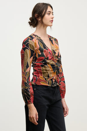 A woman wears the SYDNEY TOP by Velvet by Graham & Spencer—a long-sleeve printed cotton cambric blouse with gathered front and V-neck—paired with black jeans, standing against a plain light background.