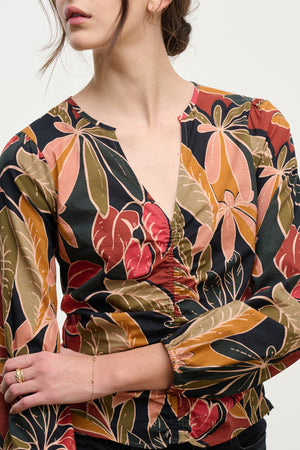 The SYDNEY TOP by Velvet by Graham & Spencer features a V-neckline, long sleeves, a ruched front, and a vibrant leaf print in green, orange, and red on comfortable printed cotton cambric.