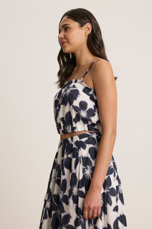 A woman stands in profile wearing the ALICE CAMI by Velvet by Graham & Spencer, a black and white floral voile crop top with adjustable straps, paired with a matching skirt against a neutral background.