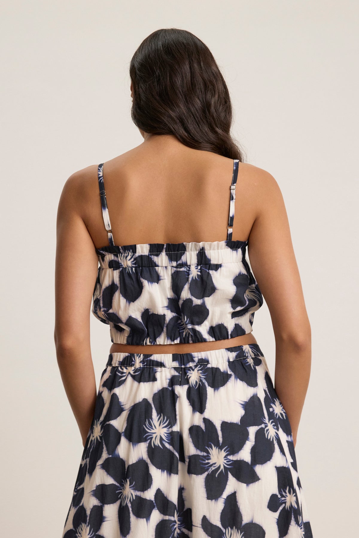 A woman is shown from the back wearing the Velvet by Graham & Spencer ALICE CAMI with adjustable straps and a matching skirt, both in a black and white floral pattern.-39123369754817