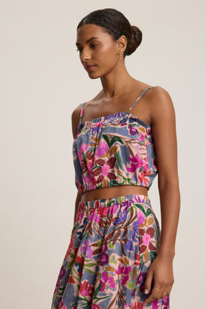 A woman wears the ALICE CAMI by Velvet by Graham & Spencer—a sleeveless, cropped cami with adjustable straps—paired with a matching floral voile skirt, standing against a plain background.