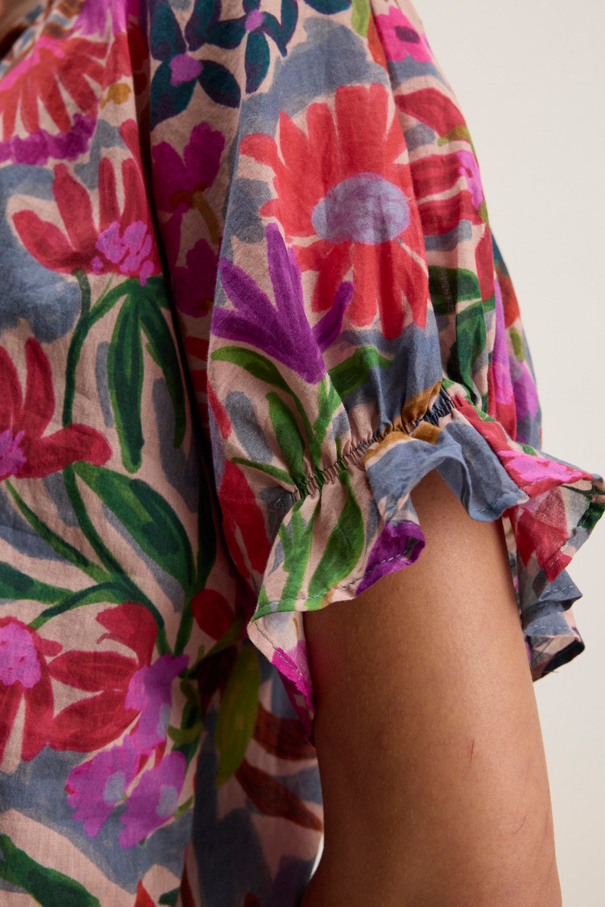 Close-up of a person's arm wearing the DELILAH BLOUSE by Velvet by Graham & Spencer, a cotton voile floral-printed top with ruffled short sleeves and elastic trim.-39111854194881