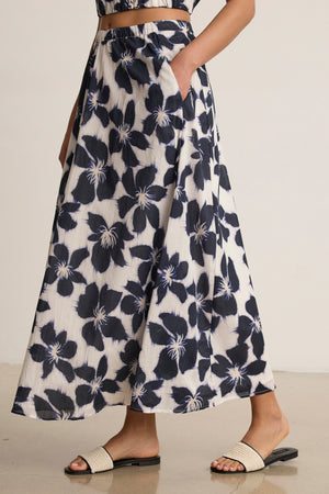 Wearing the JESS SKIRT by Velvet by Graham & Spencer, this person showcases a flowy silhouette indoors with a matching top and white slide sandals.
