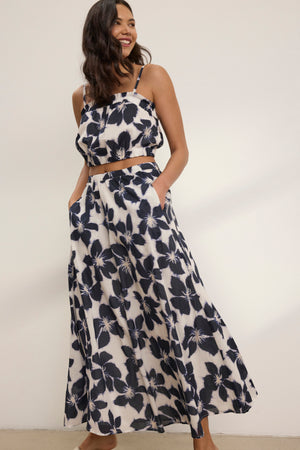 A woman stands against a plain background wearing the JESS SKIRT by Velvet by Graham & Spencer, a black and white floral print maxi with pockets and a flowy silhouette reminiscent of printed voile.