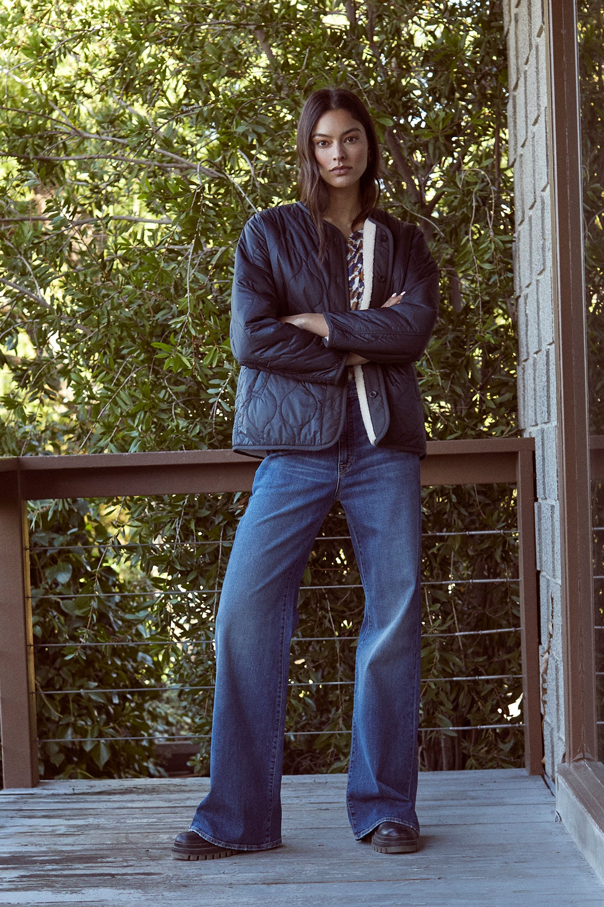 A woman is standing on a cozy porch with her arms crossed wearing the MARISSA REVERSIBLE QUILTED SHERPA JACKET by Velvet by Graham & Spencer.-35224506138817