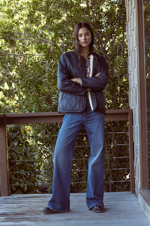 A woman is standing on a cozy porch with her arms crossed wearing the MARISSA REVERSIBLE QUILTED SHERPA JACKET by Velvet by Graham & Spencer.