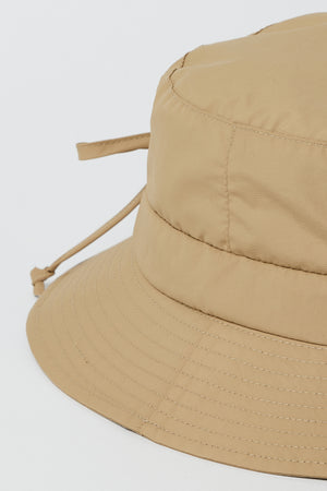 Close-up of the RAIN HAT by Velvet by Graham & Spencer, a light brown, water-resistant 100% nylon bucket hat with visible stitching and an adjustable back drawstring, set against a plain white background.